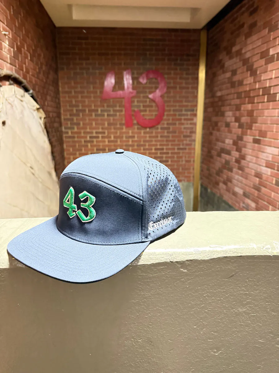 Light blue cap embroidered with a green "43", resting against a firehouse wall