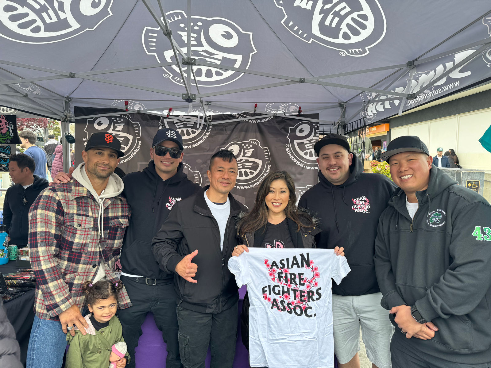 Asian Firefighters Association members at an event tent holding up a shirt
