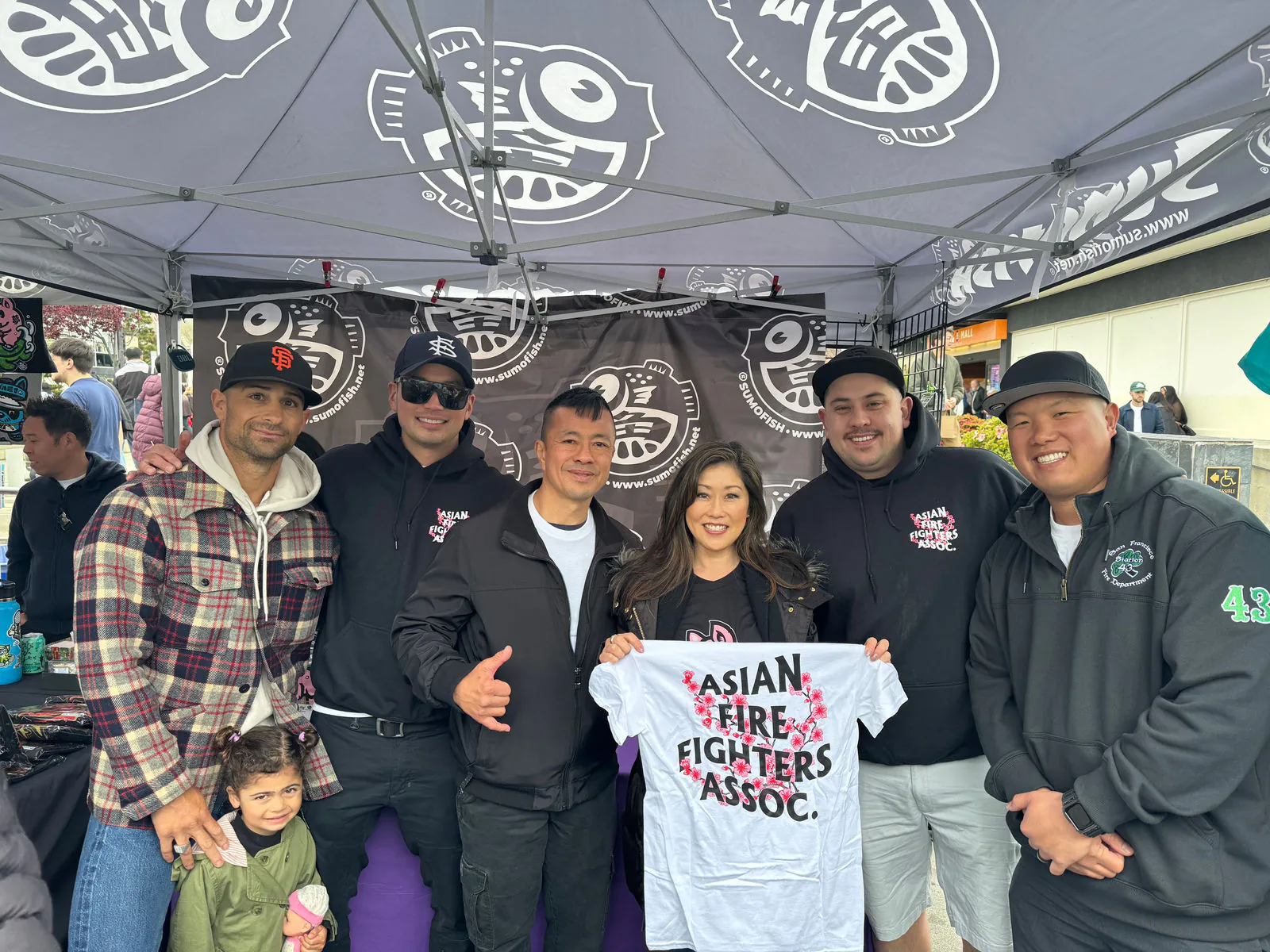 Asian Firefighters Association members at an event tent holding up a shirt