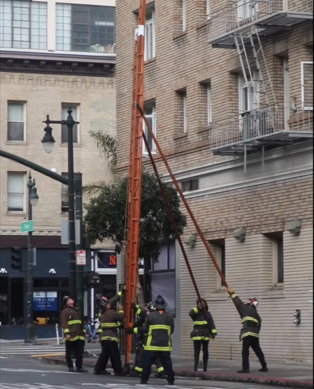 A crew raising a ground ladder to the upper floors of a city building